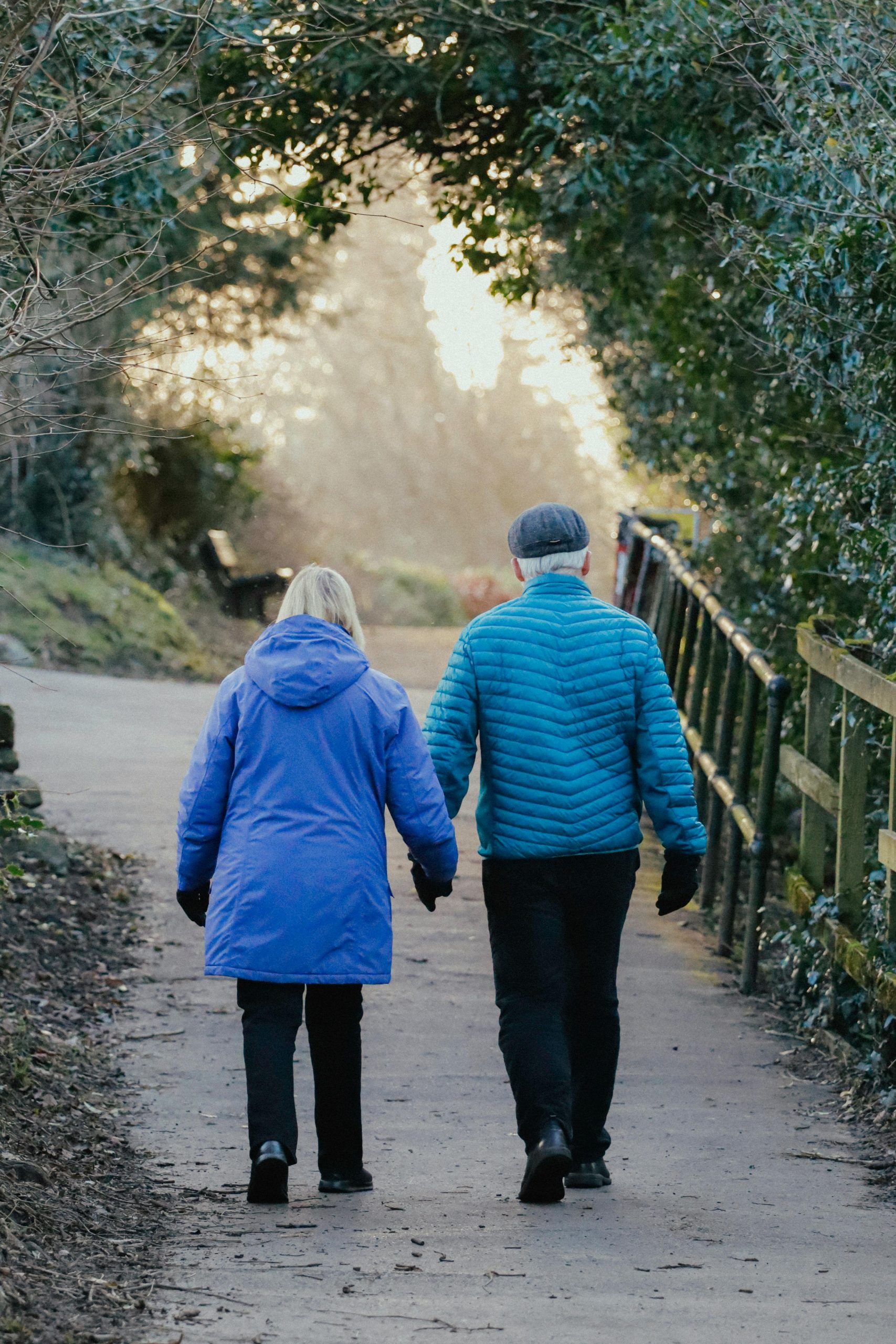 Older couple in warm jackets walking hand in hand on a path.