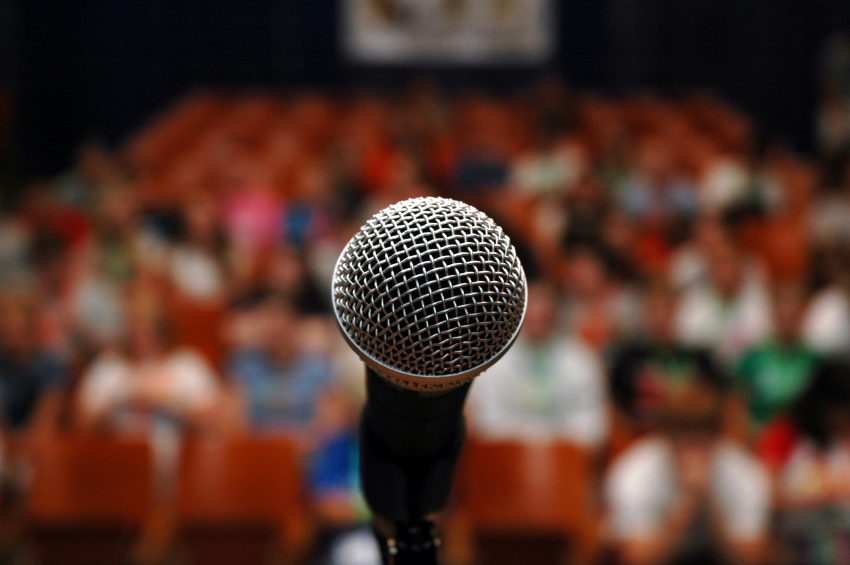 a photo showing a microphone up close with the audience blurred in the background