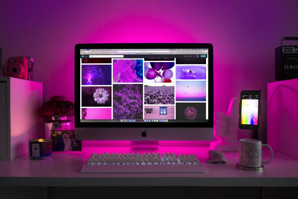 photo shows a desktop computer full of purple-themed photograph choices, and the desk around the computer has ambient pink lighting and interesting design touches like a large white thumbs up statue