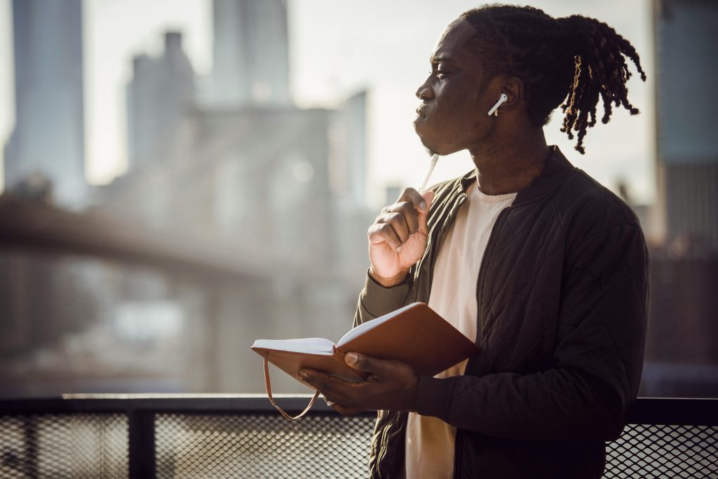 photo of a person holding an open journal and a pen and staring off in thought