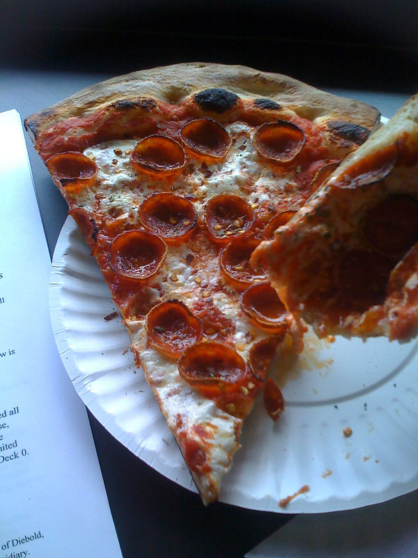 a pepperoni pizza slice on a paper plate with the type of cupped pepperonis mentioned above and a second held in the air with a bite out of it
