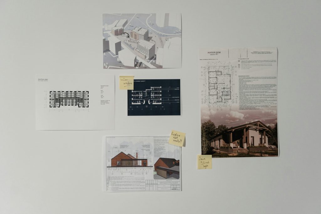 a photo of architectural drawings on a wall showing various stages of the building process, some with post-it notes asking questions