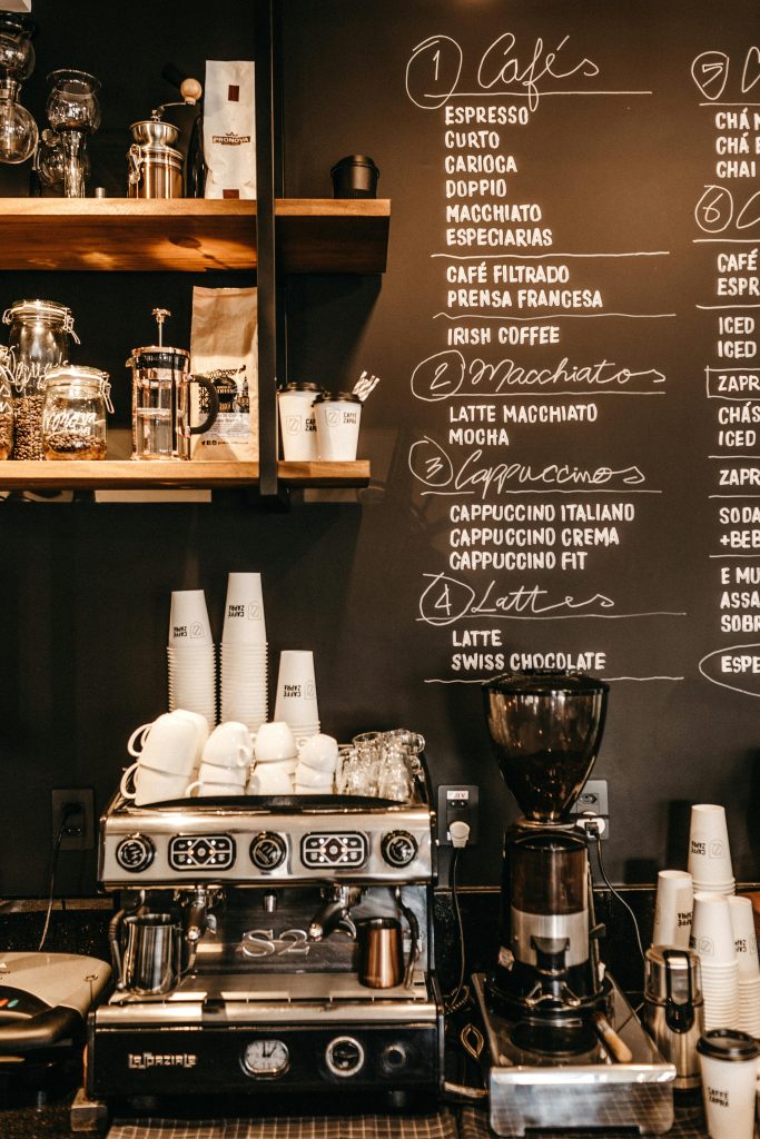 a photo of a complex espresso machine stacked with multiple sizes of cups and mugs with a menu behind it detailing various types of machiatos etc